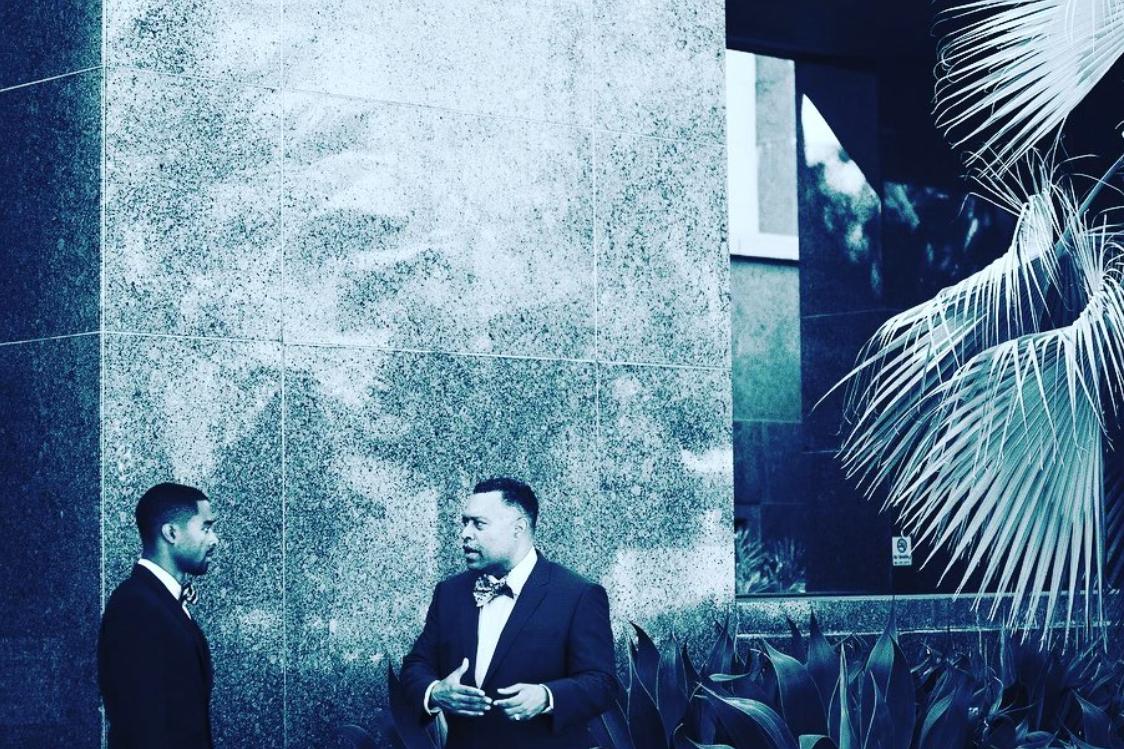 Arnold Reed and Arnold Reed II speaking in front of the courthouse in a filtered photo with a blue overlay.