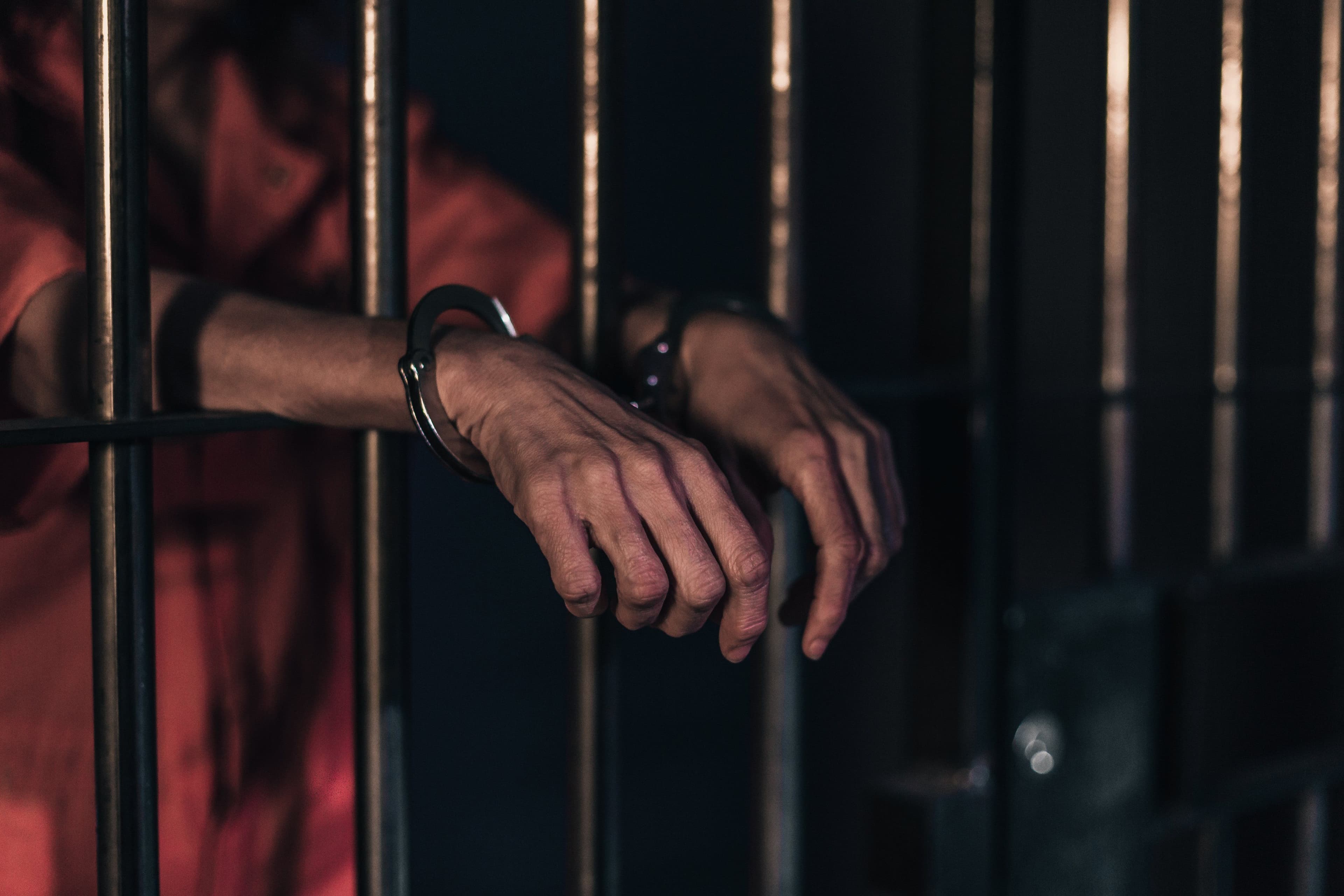The hands of a prisoner resting on the bars of a cell